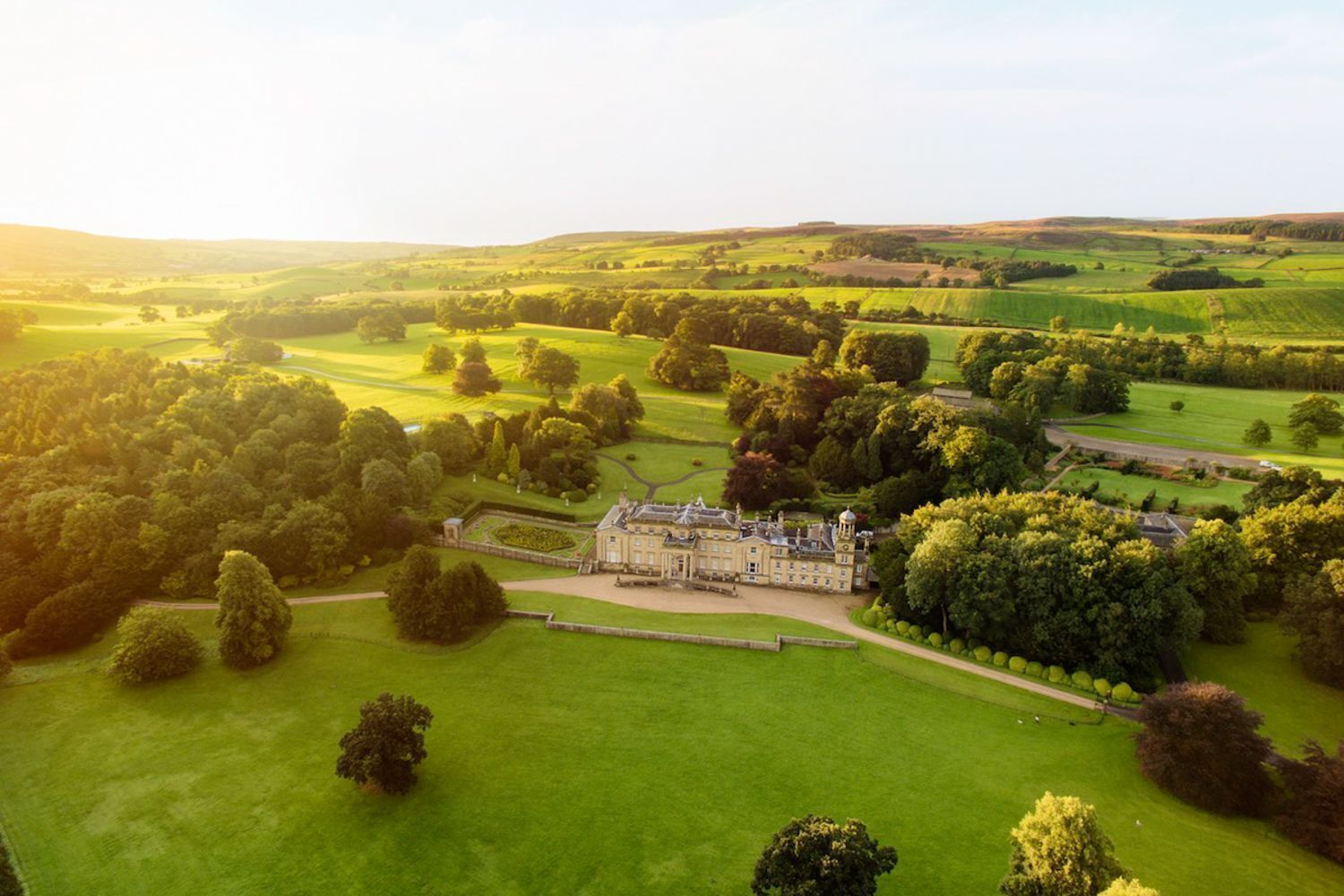 Un vaste domaine comprenant de grandes prairies verdoyantes et un bâtiment imposant à la façade symétrique.
