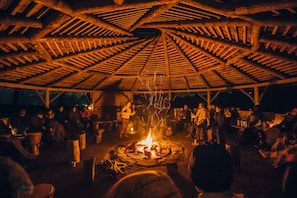 Une réunion en plein air autour d’un foyer, avec une structure en bois au-dessus.