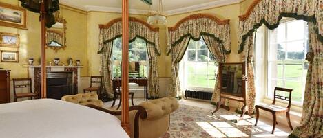 A traditional bedroom with a four-poster bed, a fireplace, and a view of the garden.