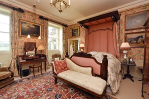 Une chambre à coucher de style traditionnel, avec un lit à baldaquin, un bureau doté d’un miroir et une chaise.