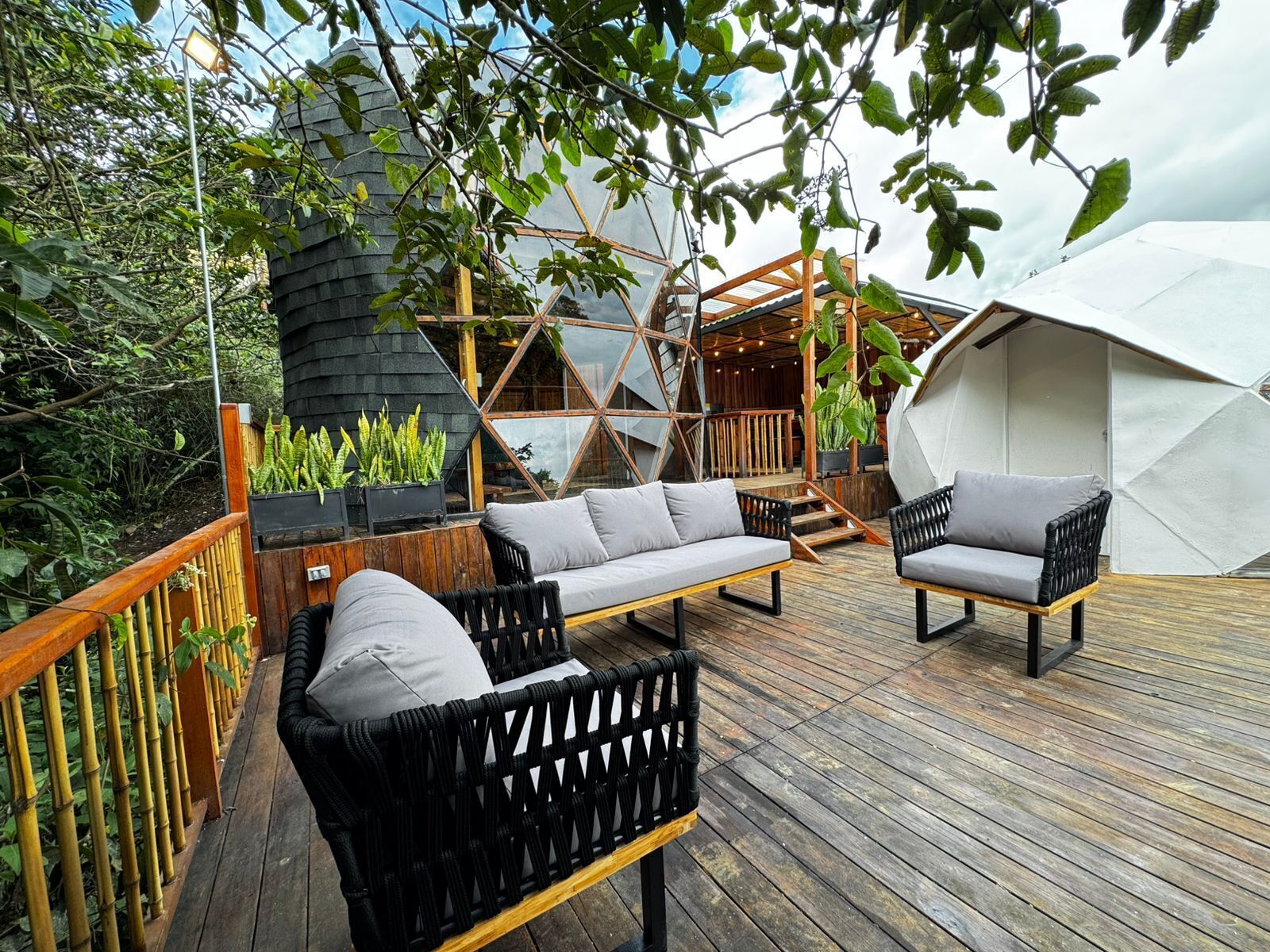 A wooden deck with outdoor furniture, a large tent structure, and a building with a sloped roof.