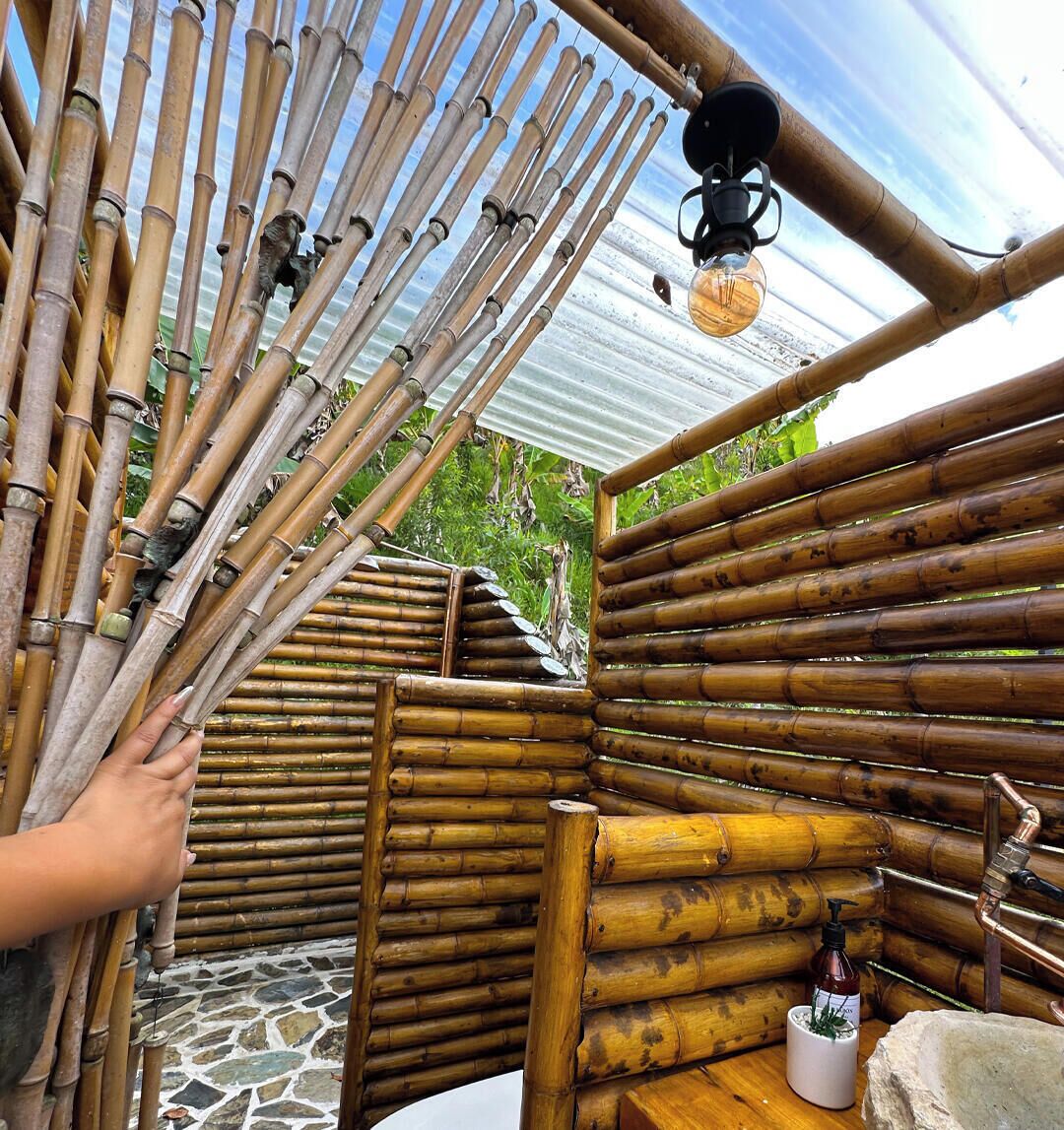 Une structure en bambou avec un sol en pierre, un luminaire suspendu et un petit pot blanc contenant une plante.