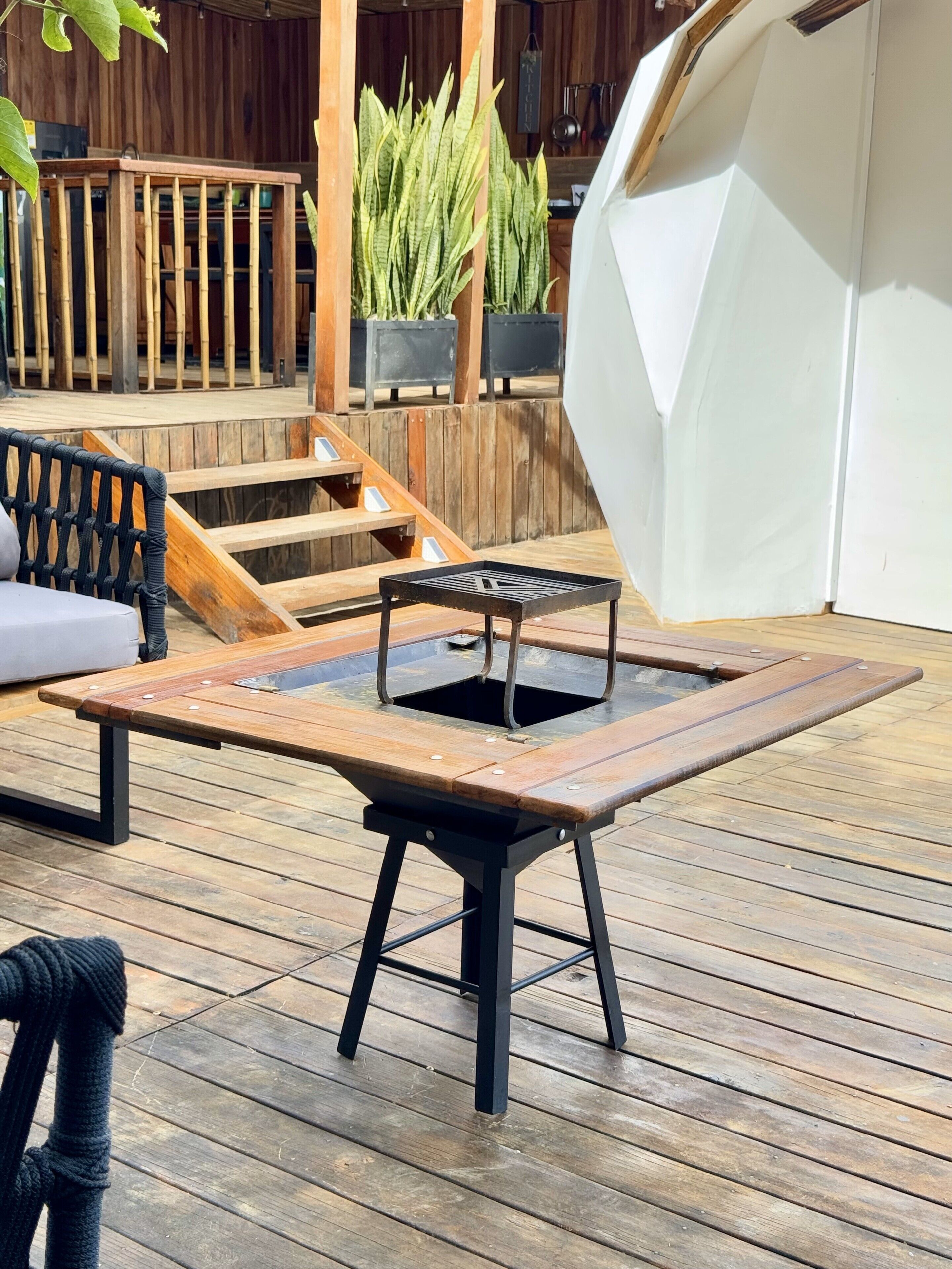 Una terraza de madera con una mesa y sillas de metal, una tienda blanca y una escalera de madera.
