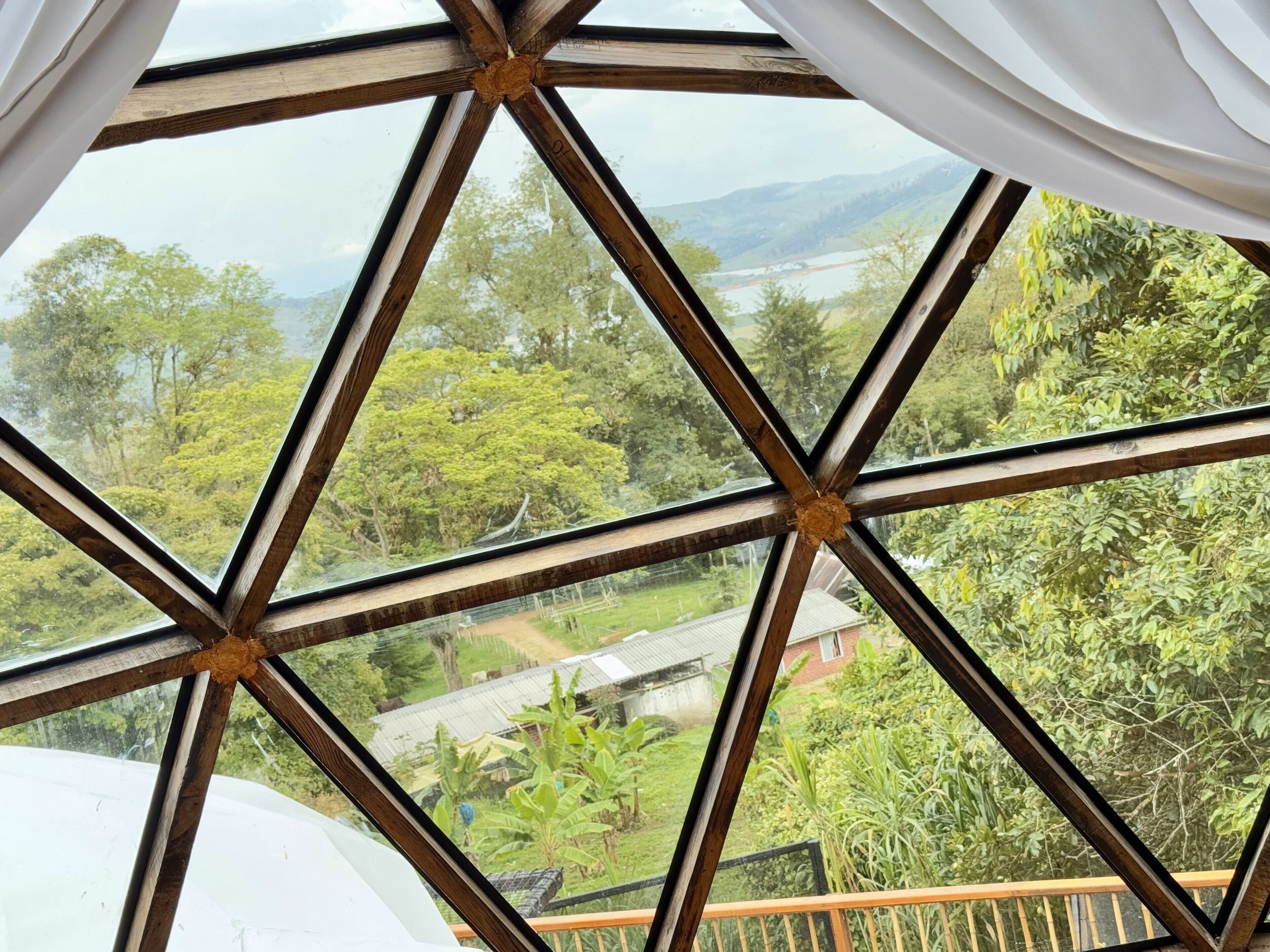 A room with a large window featuring a geometric wooden frame and white curtains.