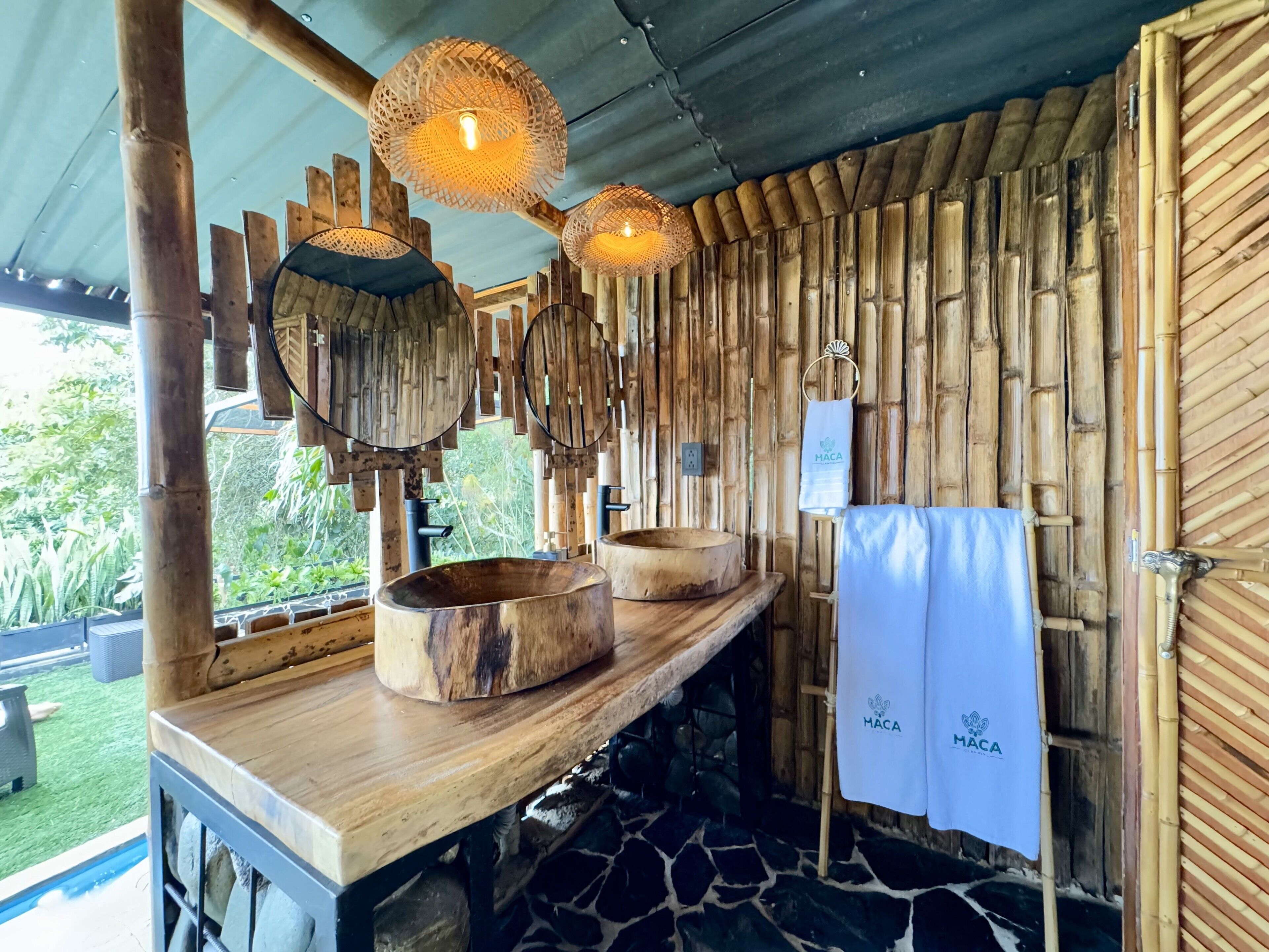 A rustic bathroom with wooden walls, a stone floor, and a wooden vanity with two basins.
