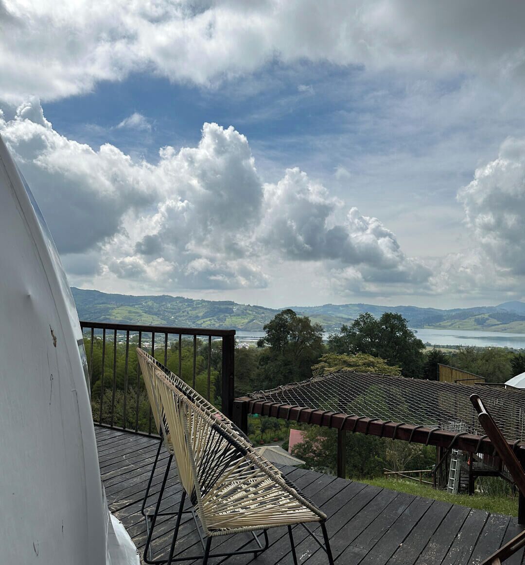 Een houten terras met een rieten stoel en een tafel, met uitzicht op een meer en heuvels.