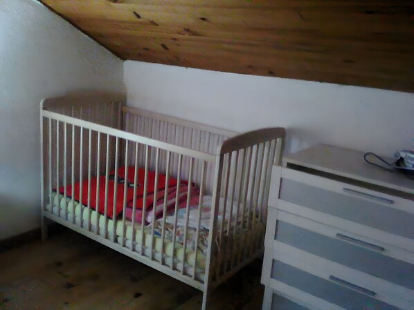 A room with a crib, a dresser, and a sloped ceiling.