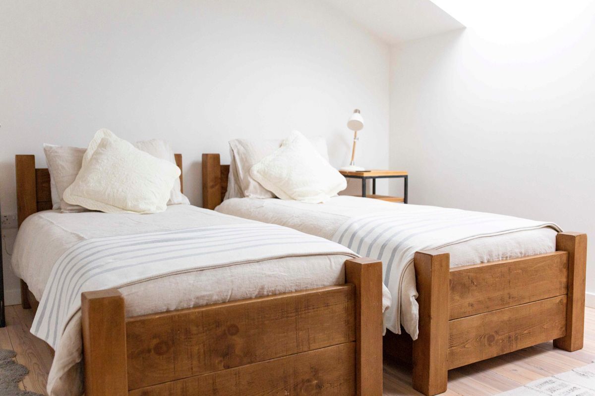 A bedroom with two wooden beds, white bedding, and a small bedside table with a lamp.