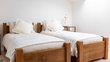 A bedroom with two wooden beds, white bedding, and a small bedside table with a lamp.