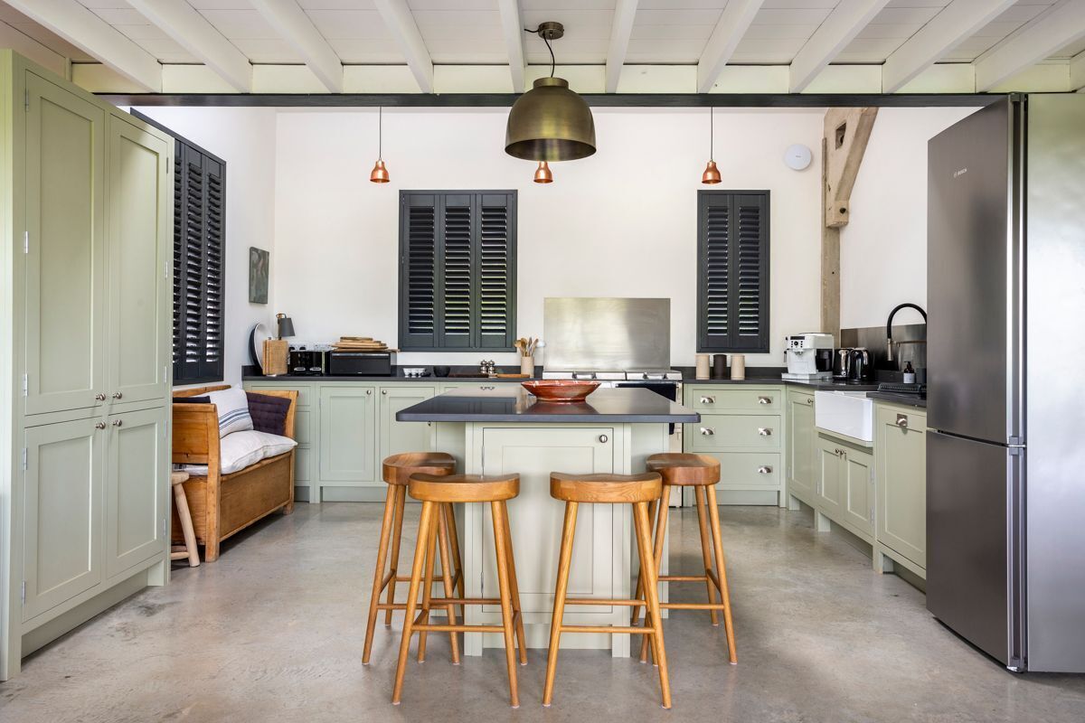 A kitchen with a central island, wooden stools, and a stainless steel refrigerator.
