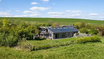 A two-story house with a sloped roof and solar panels, surrounded by a fenced yard and lush greenery.