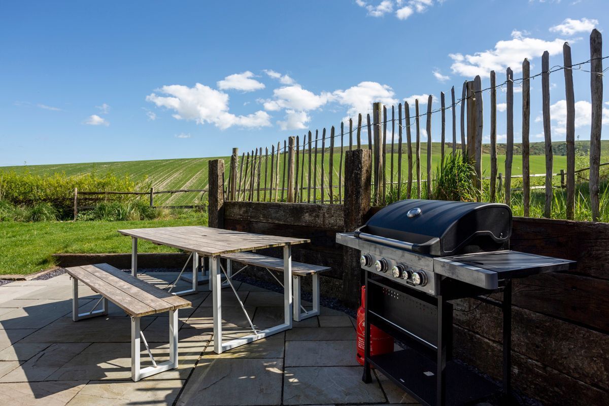An outdoor patio with a barbecue grill and picnic tables.