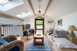A cozy living room with a high ceiling, a wooden table, and a view through a door to an outdoor area.