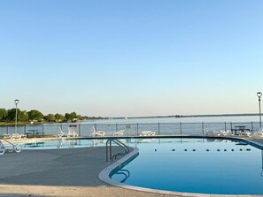 Una piscina con vista sull'acqua, circondata da una recinzione e dotata di lettini.