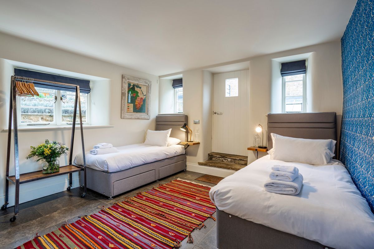 A hotel room with two beds, a window with a view, a bedside table with a lamp, and a patterned rug.