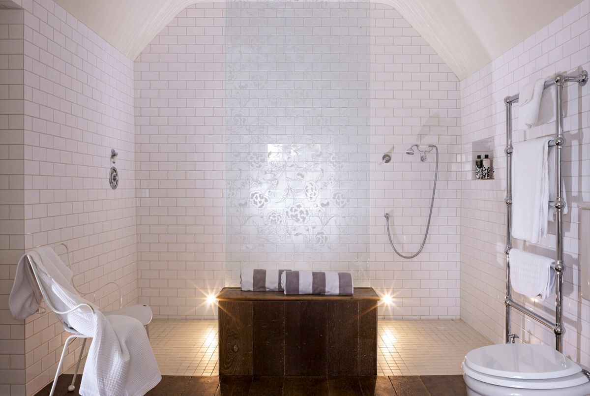 Ein Badezimmer mit weiß gefliesten Wänden, einer Holzbank, einer weißen Toilette und einer Duschkabine.