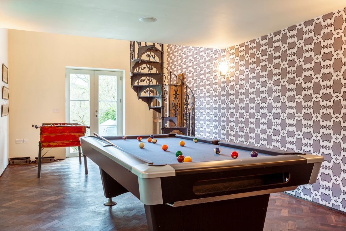 A pool table in a room with patterned wallpaper and a red sofa.