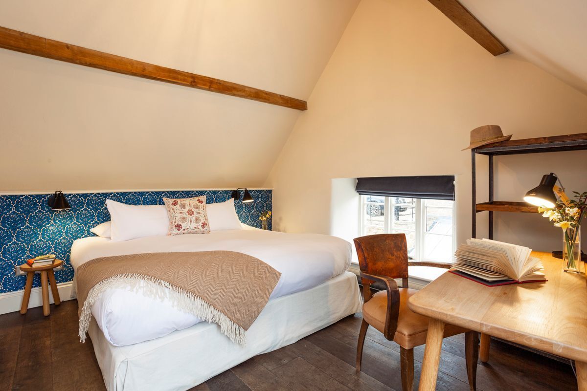 Ein Schlafzimmer mit einem großen Bett, einem Holzstuhl, einem kleinen Tisch mit Büchern und einem Fenster.