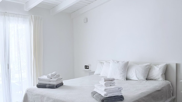 Una camera da letto minimalista con un letto grande, biancheria da letto bianca e una pila di asciugamani ben riposti.