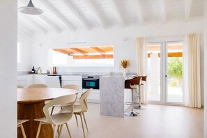 A modern kitchen with a dining area, large windows, and a view of greenery outside. - Villa Alora Lux - Two Bedroom Villa, Sleeps 6 (Álora)