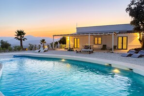 Et moderne hus med swimmingpool, udendørs møbler og udsigt til bjerge.