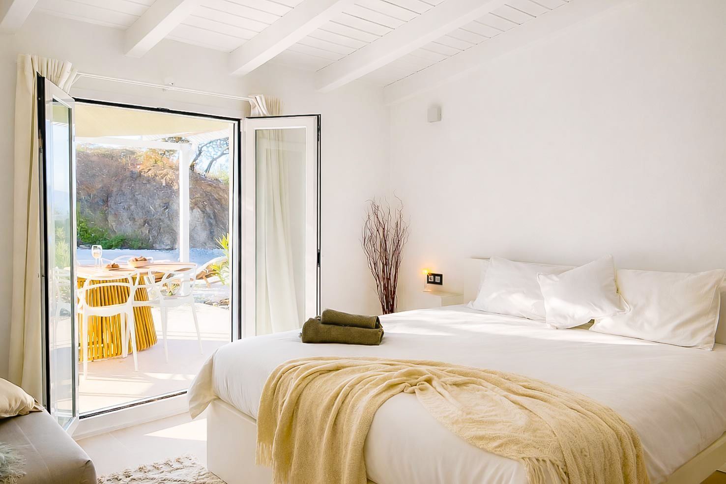 A bedroom with a bed, a nightstand, a lamp, and a view of an outdoor dining area.