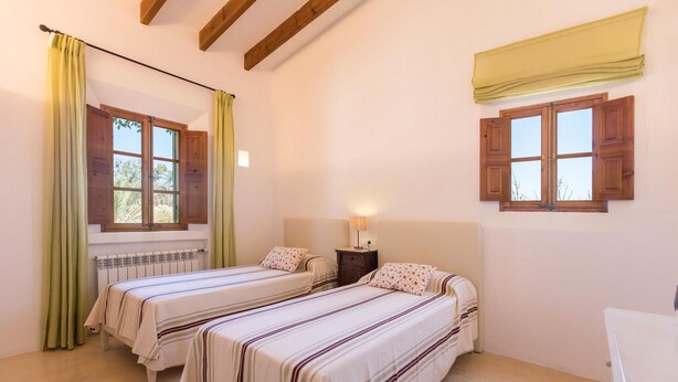 Ein Zimmer mit zwei Betten, einem Nachttisch, einer Lampe, einer Heizung und einem Fenster mit Holzklappläden.