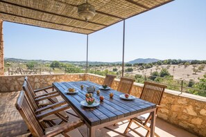A wooden table set with plates of fruit and a hanging light fixture in a stone-walled outdoor area with a view of the countryside. - Casa Begura - Two Bedroom Villa, Sleeps 4 (Mallorca)
