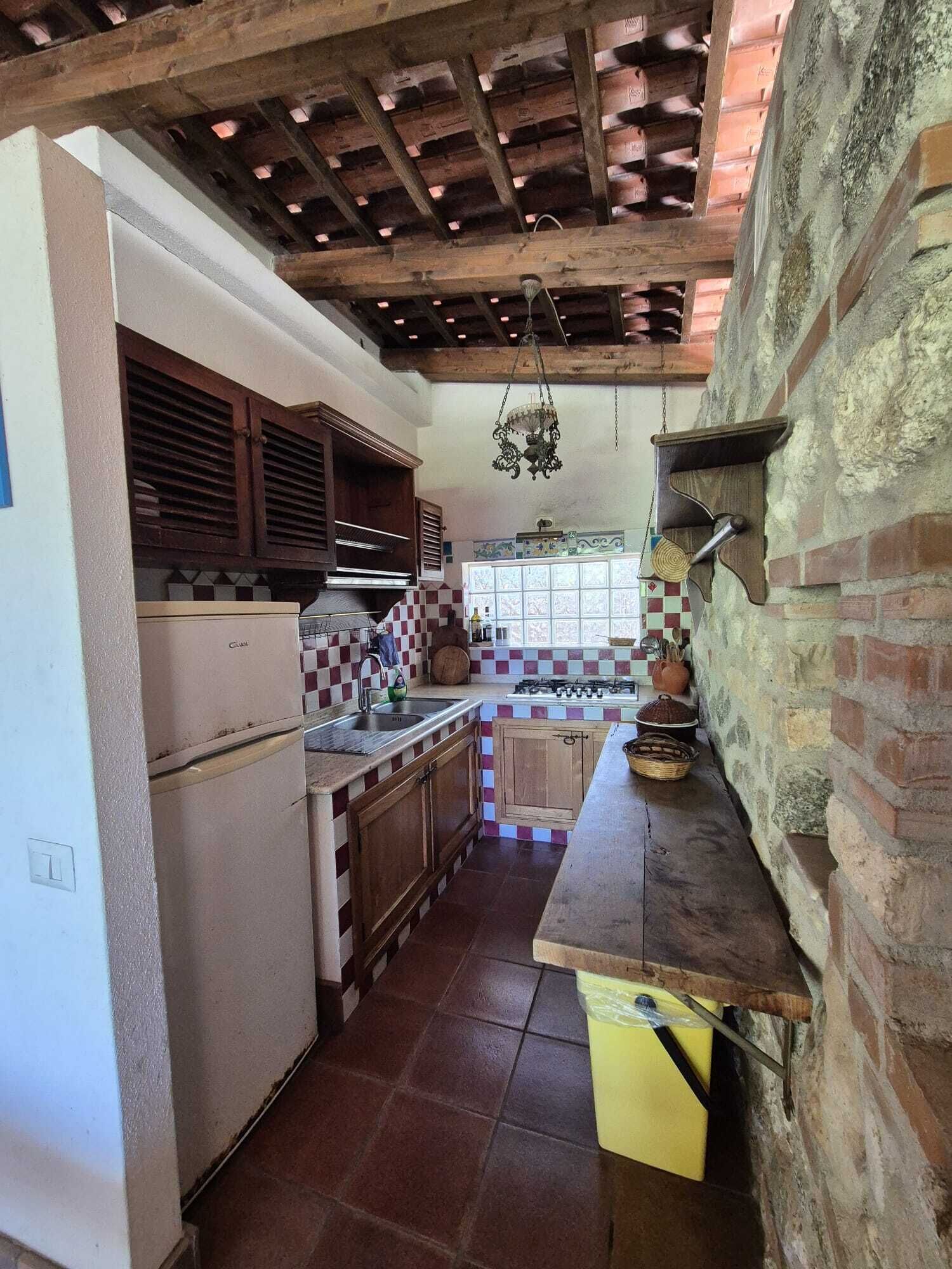 A kitchen with a wooden ceiling, a gas stove, and a window with checkered tiles.