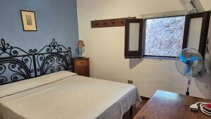 Ein Schlafzimmer mit Bett, Nachttisch, Lampe, Fenster und Deckenventilator.
