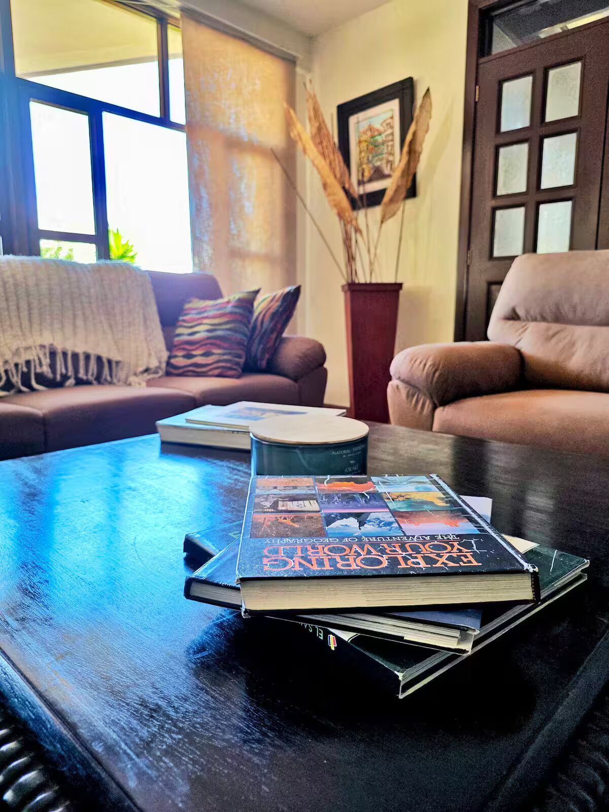 Ein Wohnzimmer mit einer Couch, einem Couchtisch mit Büchern und einem Fenster mit Tageslicht.