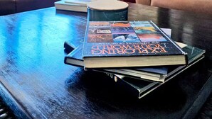 Een woonkamer met een bank, een bijzettafeltje met boeken en een raam met daglicht.