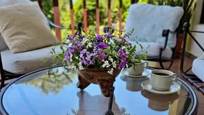 Een ronde glazen tafel met een bloevas en een kop koffie, geplaatst op een balkon met tuinmeubilair.