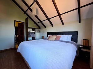 A bedroom with a large bed, a wooden ceiling, and a nightstand with a lamp.