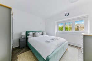 A bedroom with a bed, bedside table, lamp, and a window with a view.