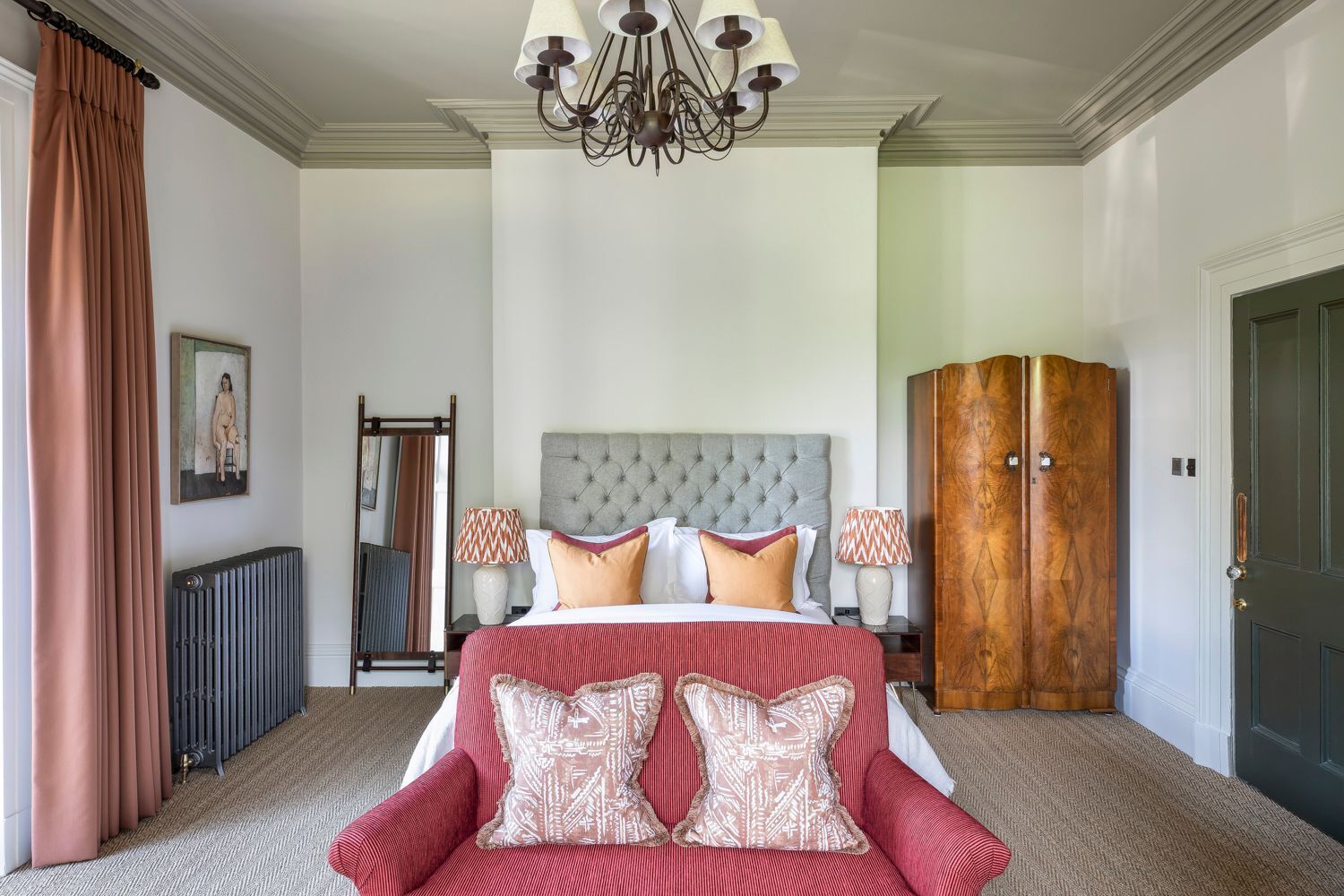A hotel room with a large bed, a red sofa, a wooden wardrobe, a chandelier, and a radiator.