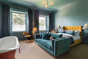 A room with a bed, a sofa, a chair, a lamp, and a window with curtains.