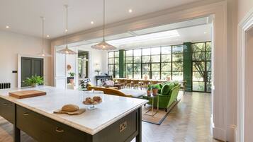 A spacious kitchen with a large island, dining area with green sofas, and a view through large windows.
