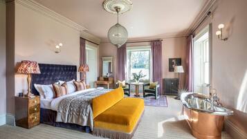 A bedroom with a large bed, a sitting area, a vanity with a mirror, and a bathtub.