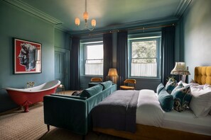 A bedroom with a large bed, a red bathtub, two chairs, a lamp, and a painting on the wall. - Willowdale House - Six Bedroom Villa, Sleeps 16 (Castle Carrock)