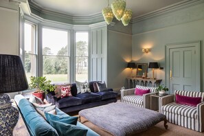 Une pièce dotée d’une grande fenêtre en saillie, d’un ensemble de canapés, d’un fauteuil à rayures et d’une table avec des lampes.