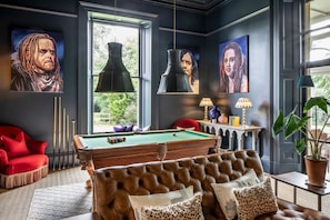 A billiards room with a pool table, red sofa, and a large window.