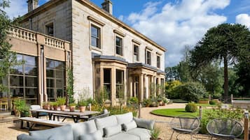 A stately stone building with a large patio area featuring outdoor furniture and potted plants.