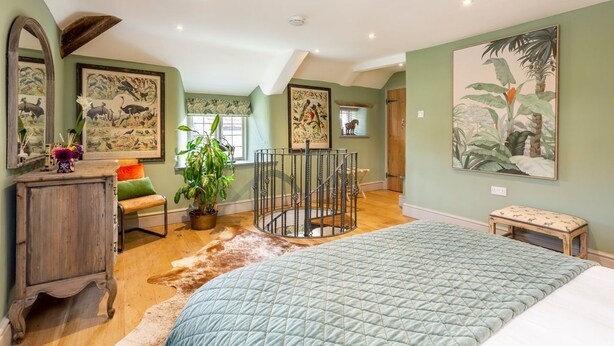A bedroom with a large bed, a wooden cabinet, a round staircase, and a potted plant.