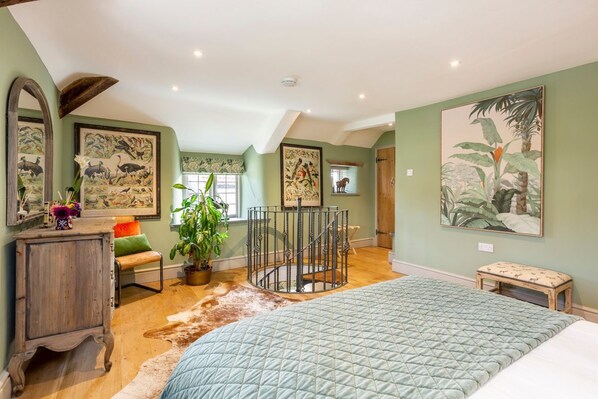 A bedroom with a large bed, a wooden cabinet, a round staircase, and a potted plant.