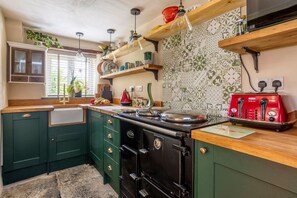 A kitchen with green cabinets, a black stove, a red toaster, and a window with plants.