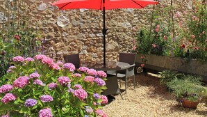An outdoor seating area with a stone wall backdrop, a table, chairs, and a red umbrella.