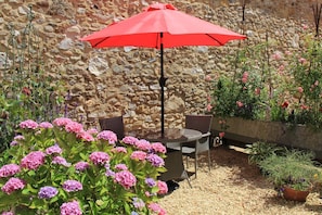 An outdoor seating area with a stone wall backdrop, a table, chairs, and a red umbrella.