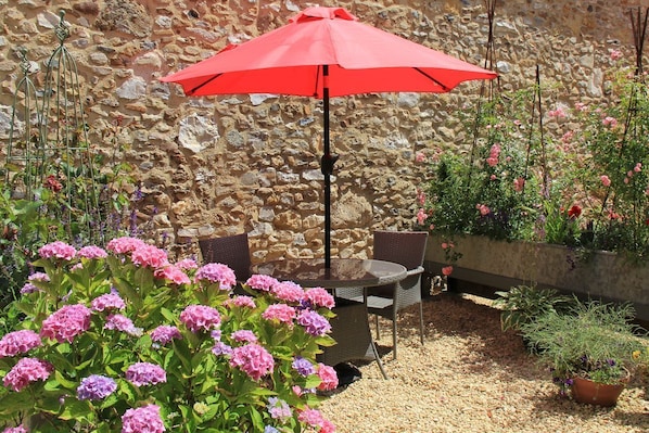 An outdoor seating area with a stone wall backdrop, a table, chairs, and a red umbrella.