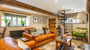 A spacious living room with a leather sofa, a wooden coffee table, and a green armchair. A spiral staircase is visible in the background.